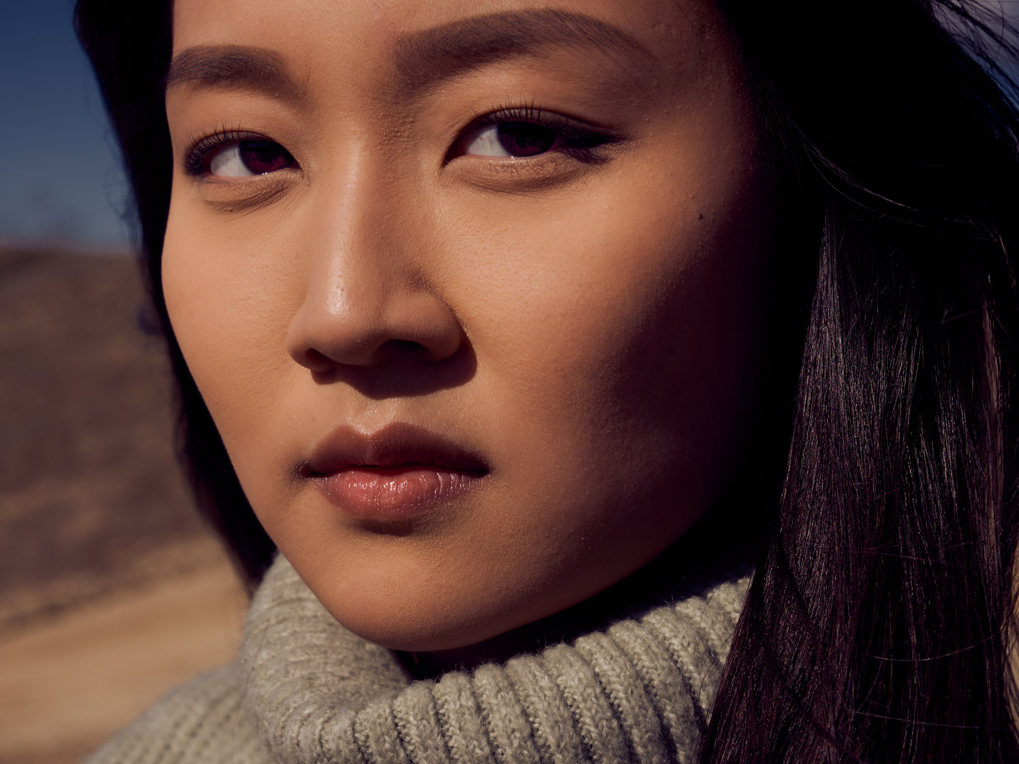 Close-up outdoor beauty portrait of a woman in natural light wearing a ribbed turtleneck sweater with a calm, focused expression