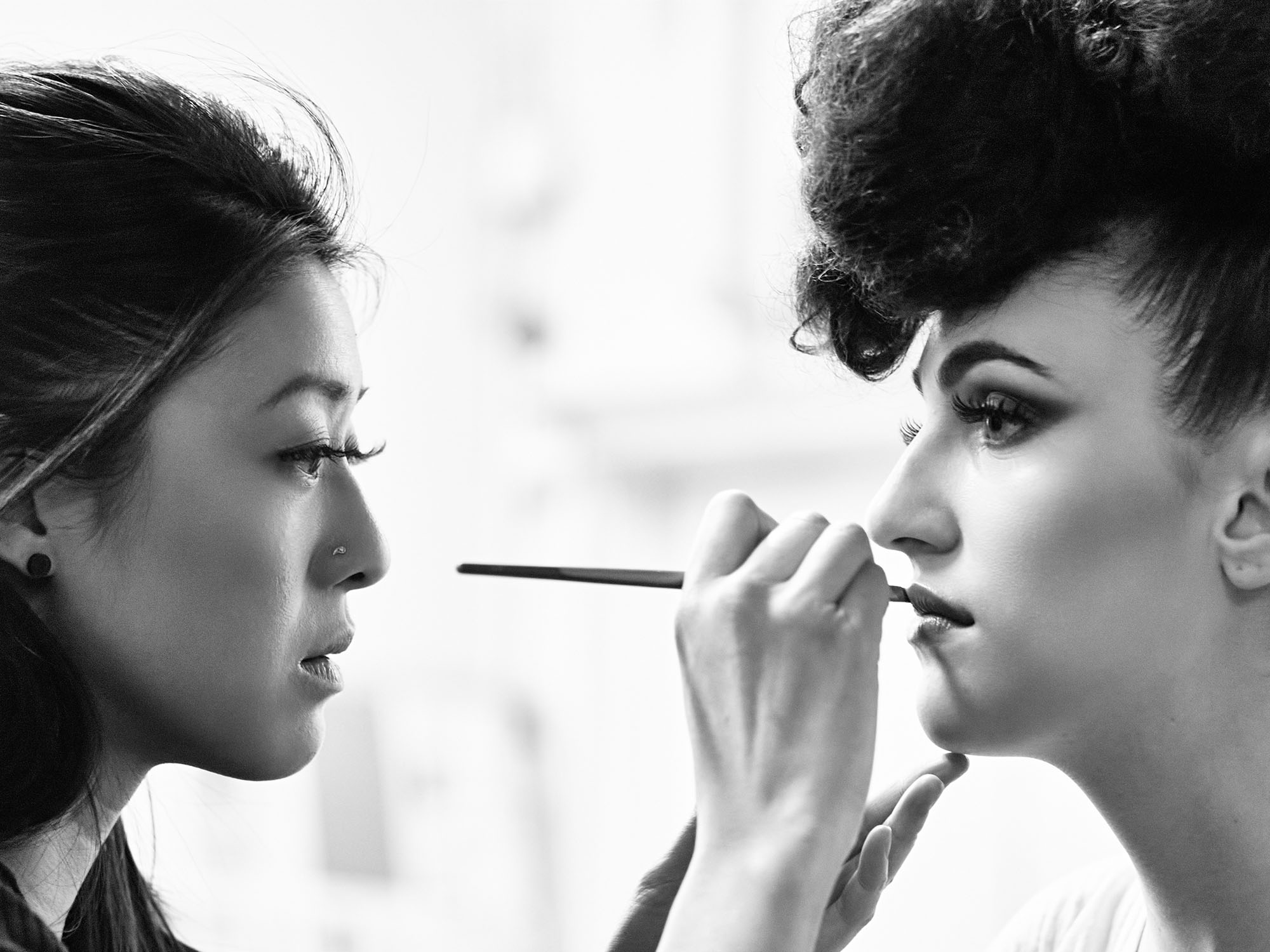 Black and white behind-the-scenes photo of makeup artist Wenya Chang applying lipstick to model Renee Vermeuel before a beauty portrait shoot