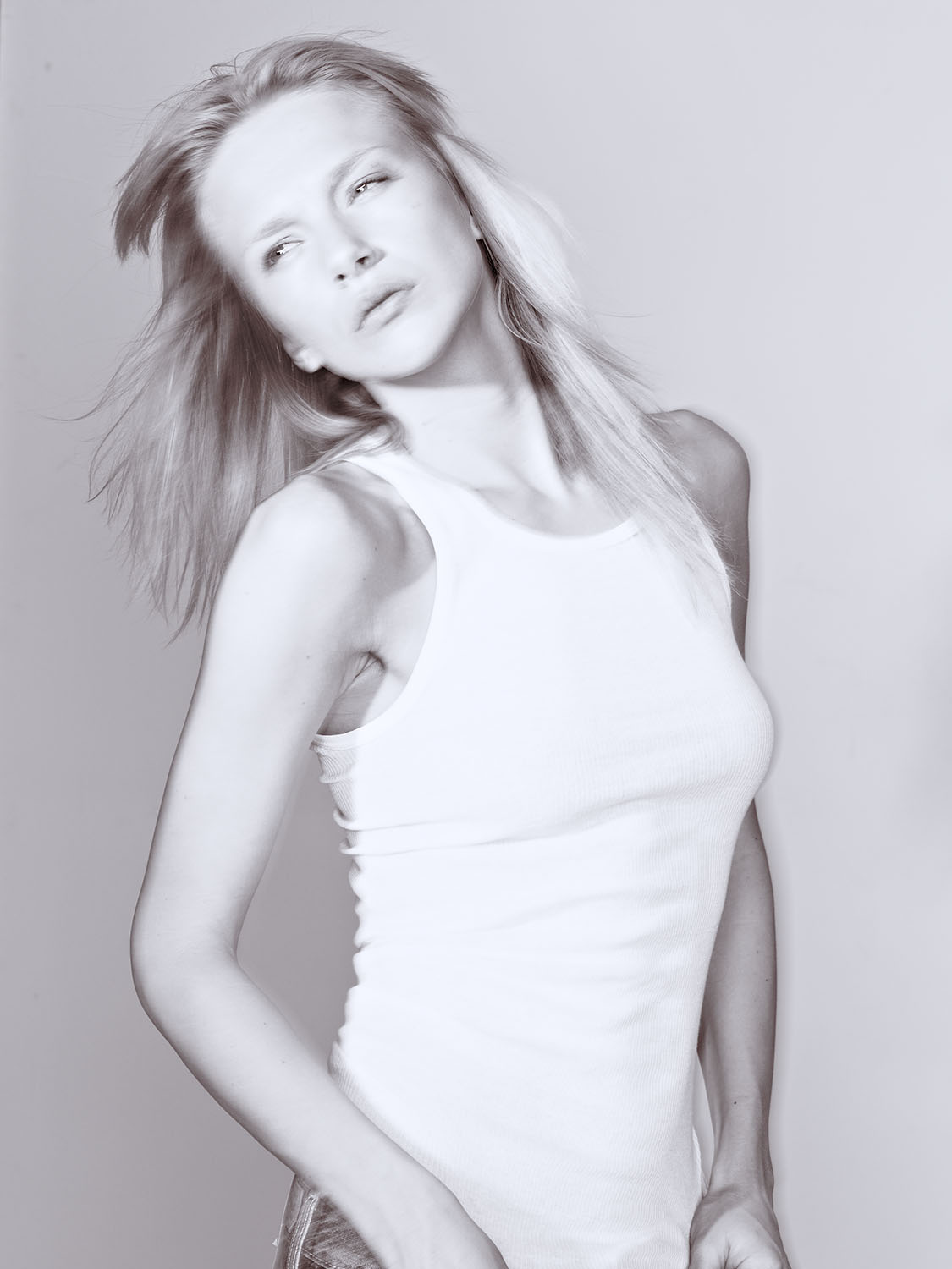 Black and white studio portrait of Oksana from MC2 Model Management NYC wearing a white tank top with flowing hair and a soft, expressive gaze