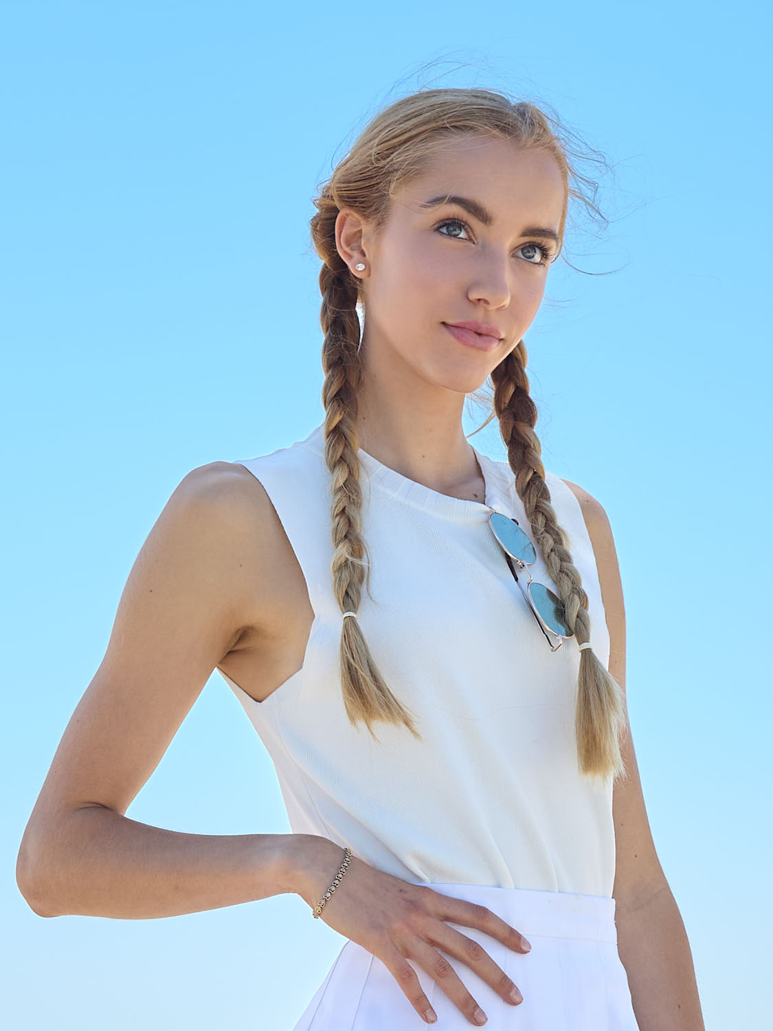 Portrait of model Elizabeth Tyler Tuls wearing a white outfit with braided hair, posing under clear blue sky in bright natural light