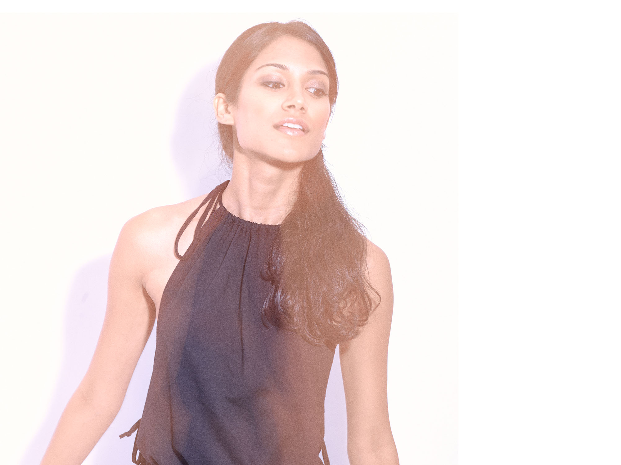 Elegant fashion editorial portrait of South Asian actress Melanie Chandra in soft lighting, wearing a black halter top with a confident and poised expression