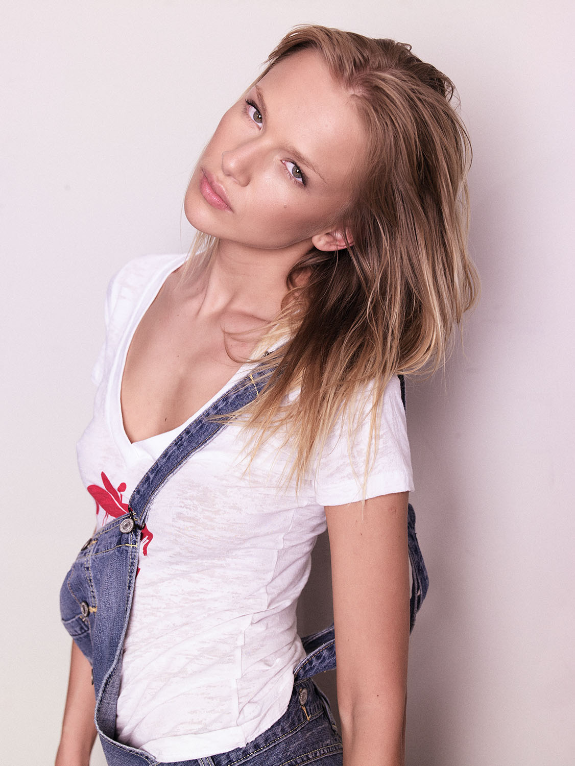 Close-up portrait of Oksana from MC2 Model Management NYC wearing denim overalls and a white tee, with natural makeup and relaxed styling